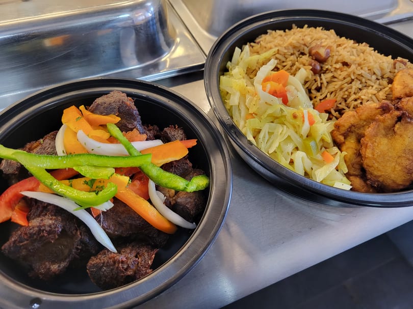 Two Haitian meals in black bowls: fried meat with peppers and rice with cabbage and plantains.