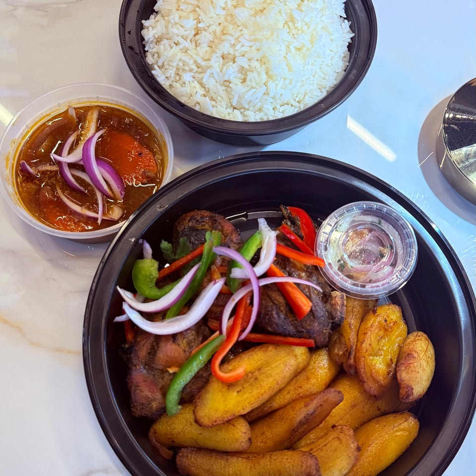 Haitian griot with fried plantains, rice, and a side of pikliz on a marble table.