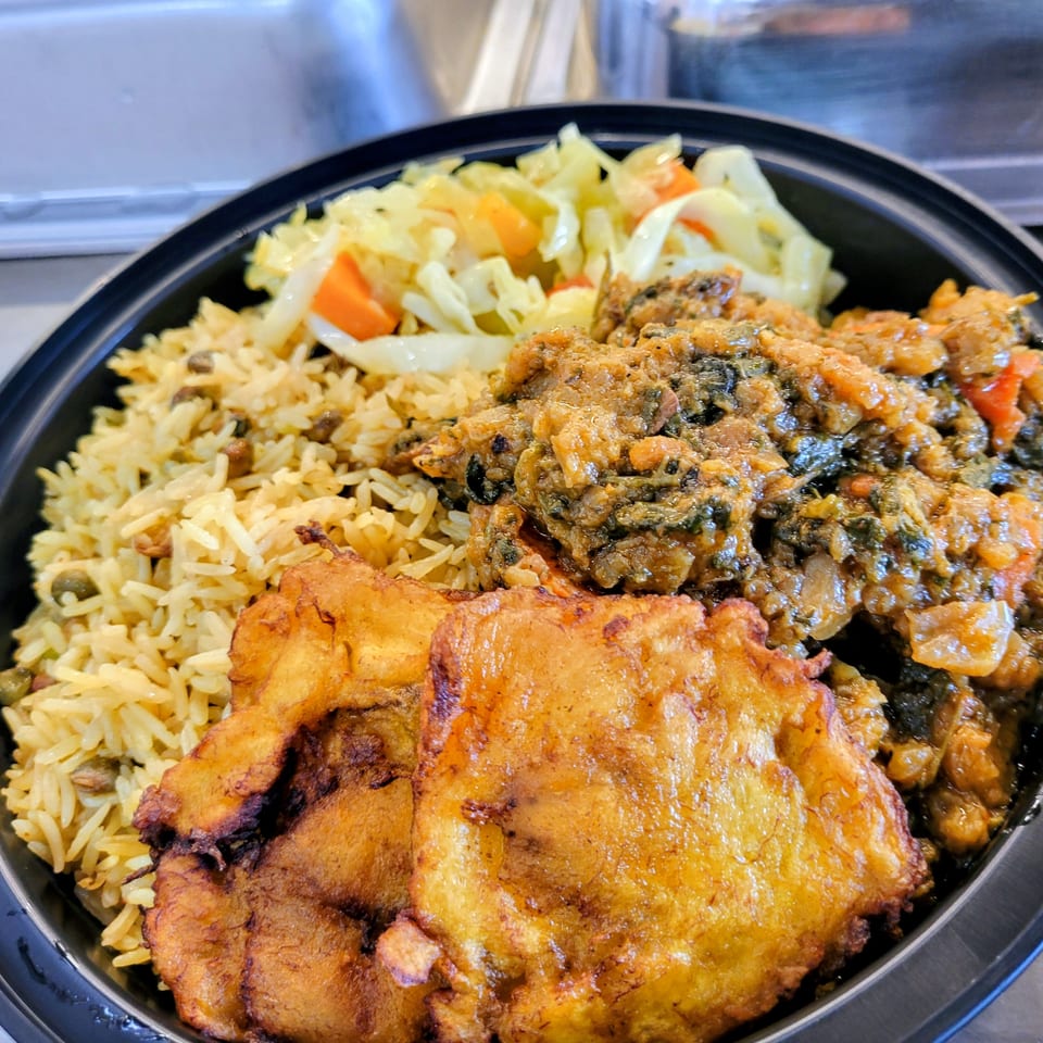Haitian meal with rice, stewed greens, fried plantains, and cabbage in a black bowl.